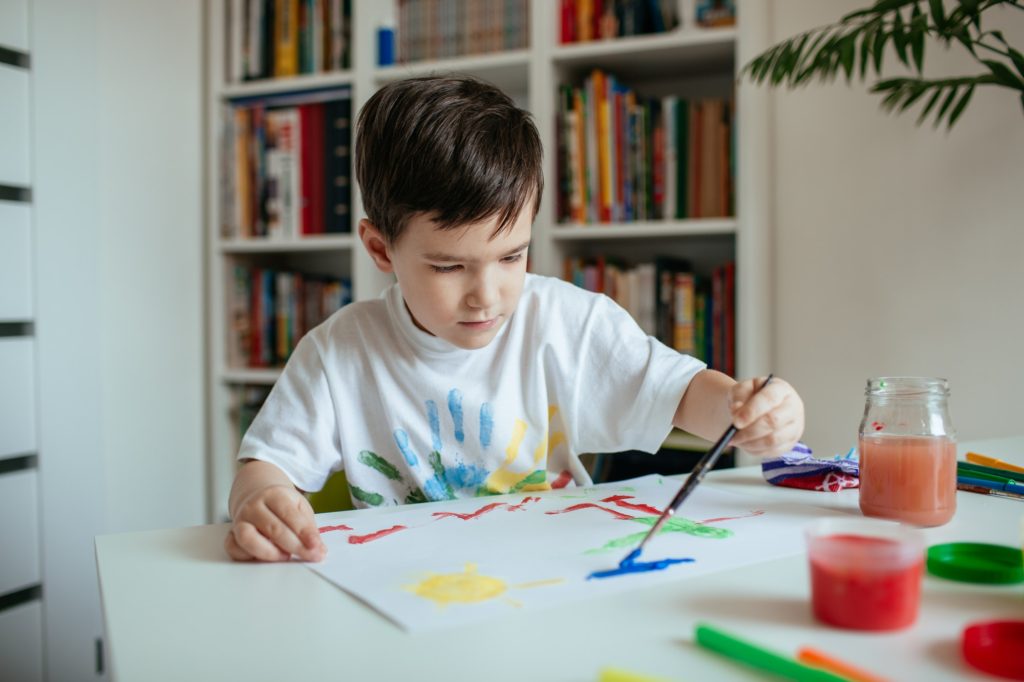 Left handed cute preschooler boy painting picture.